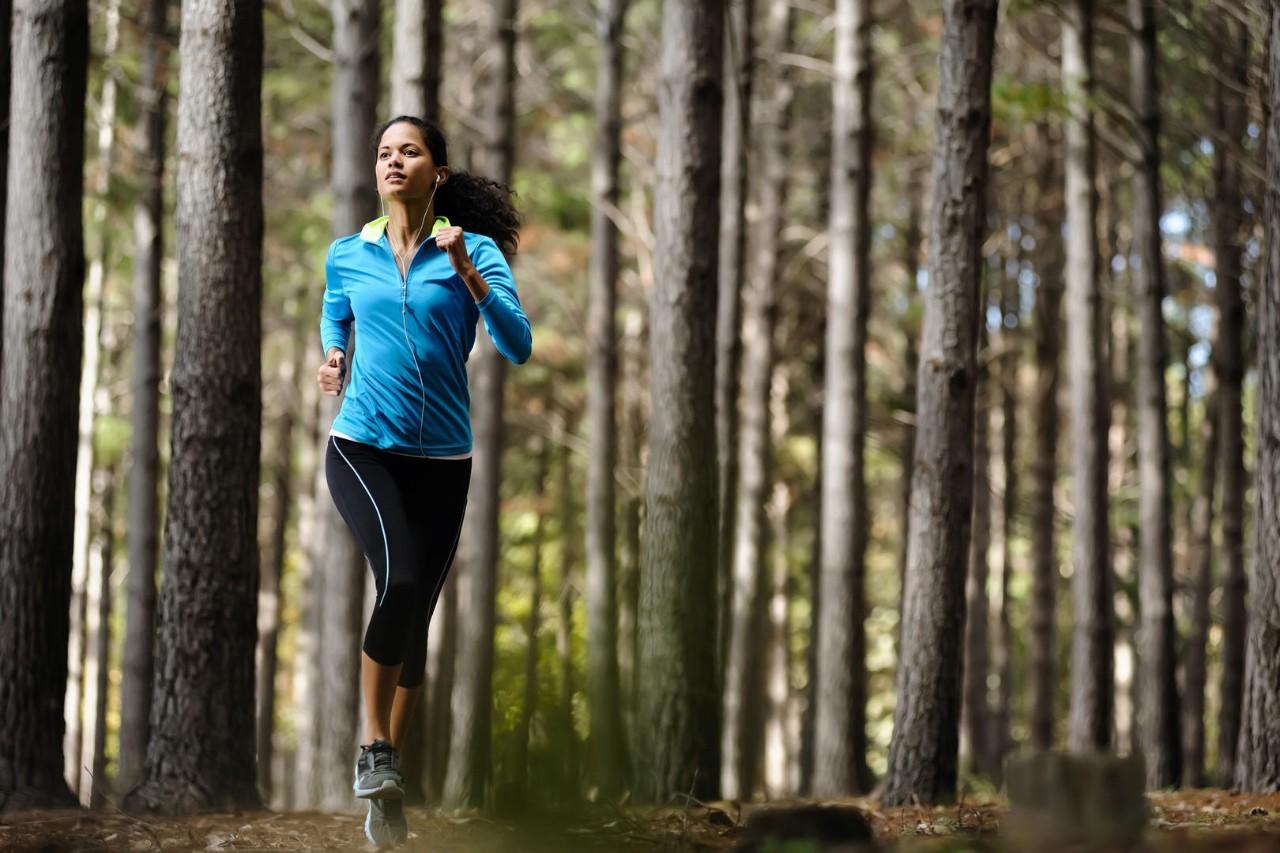 Woman running in wooded forest area, training and exercising for trail run marathon endurance