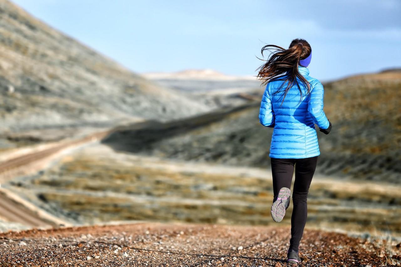 Woman winter and autumn running in down jacket on mountain trail